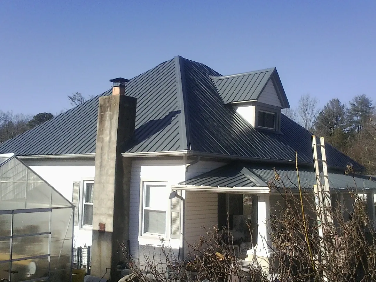 Dark blue standing seam metal roof on a white farmhouse with dormer — Slate & Tile Roof Repair by Roofing Brothers in Hallandale