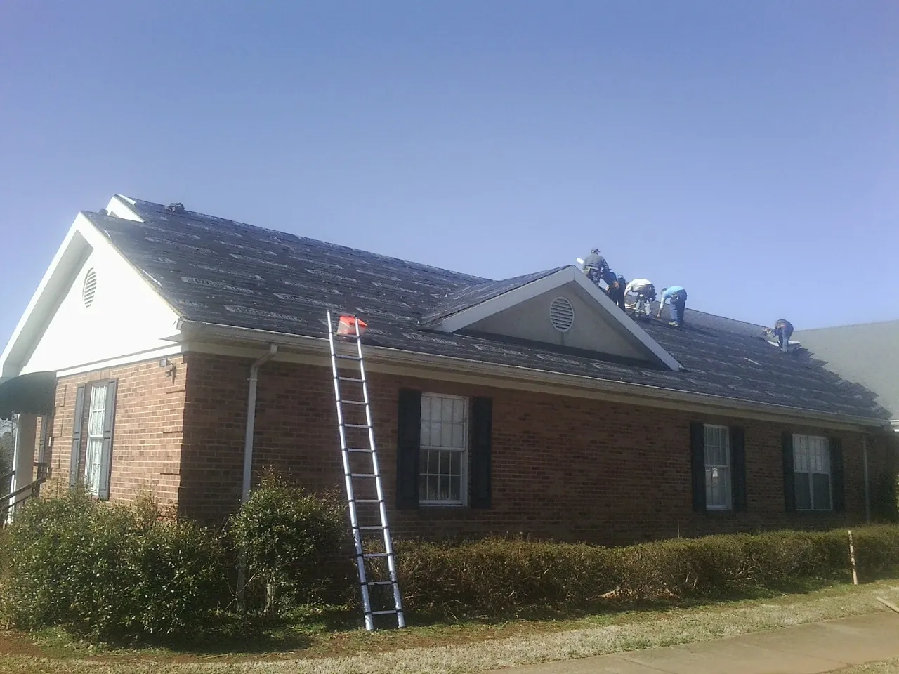 Crew tearing shingles off a brick ranch roof with a ladder set — Metal Roof Repair work by our crew in Hallandale