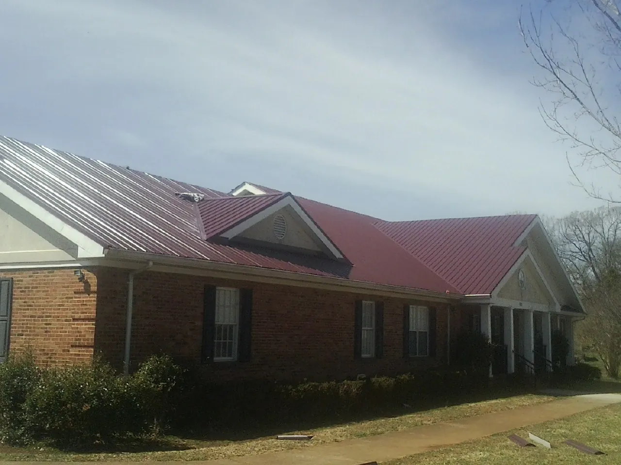 Red metal roof with gabled entries on a long brick building, from a Hail Damage Roof Repair job in Hallandale
