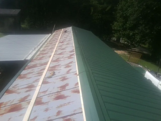 Old rusted panels beside newly installed green metal roofing — Wind Damage Roof Repair by Roofing Brothers in Hallandale