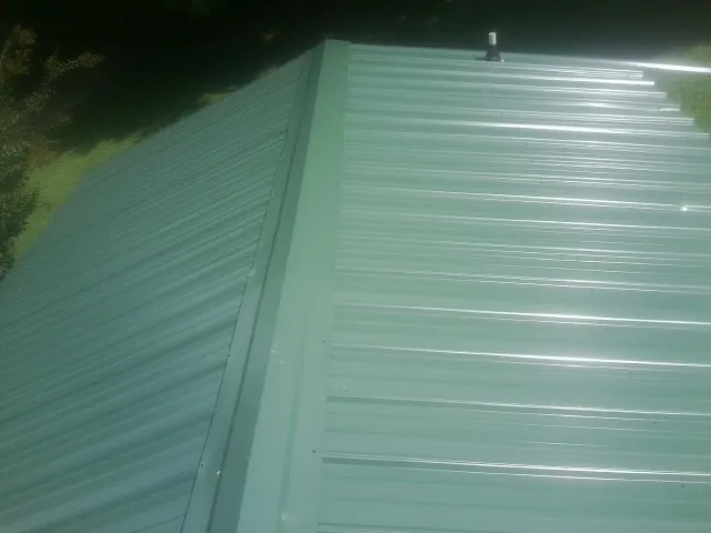 New green metal panels meeting at the ridge of a roof — Flat Roof Repair work by our crew in Hallandale
