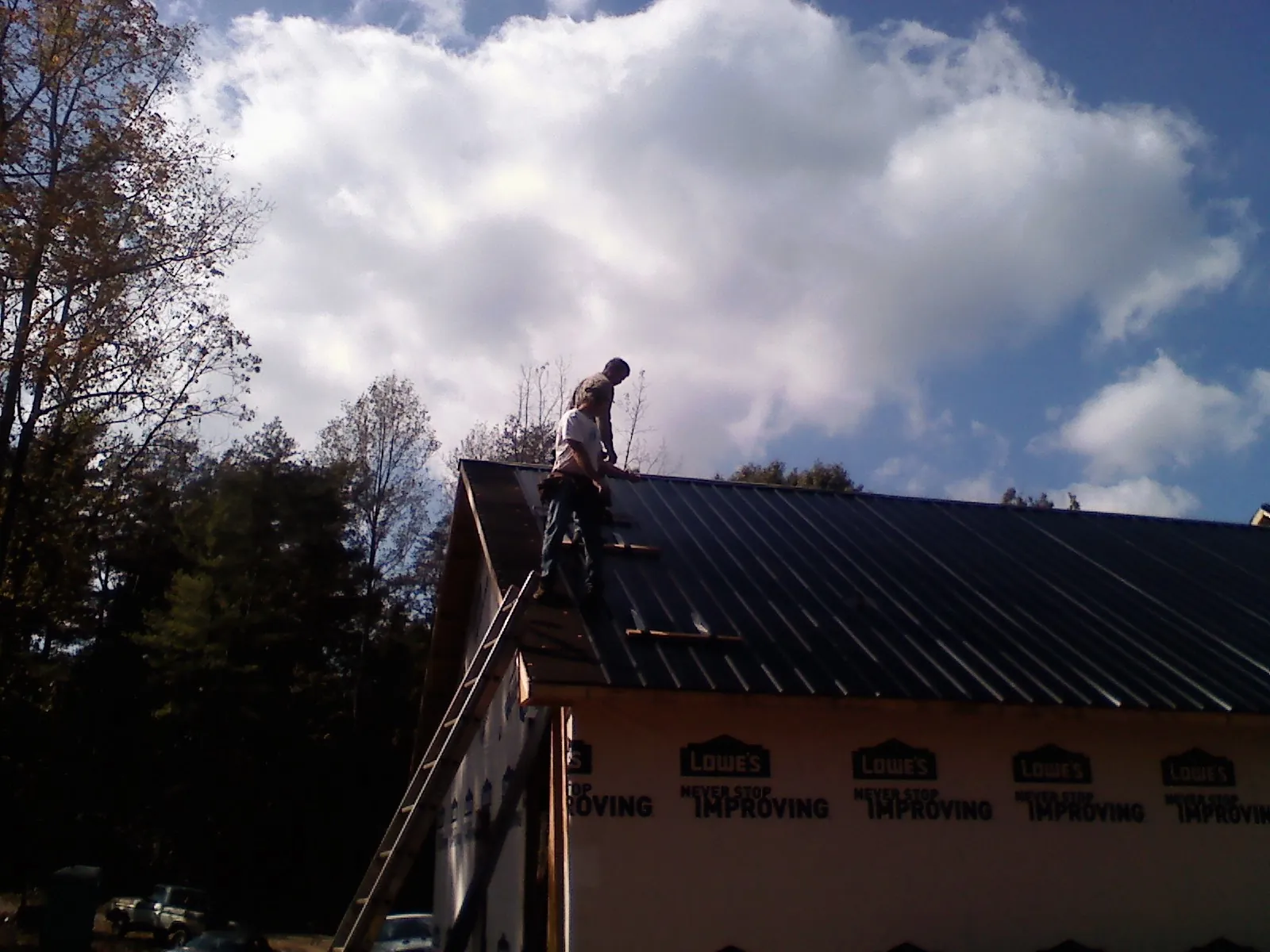 Roofer fastening dark metal panels high against a cloudy sky, from a Roof Inspection job in Hallandale